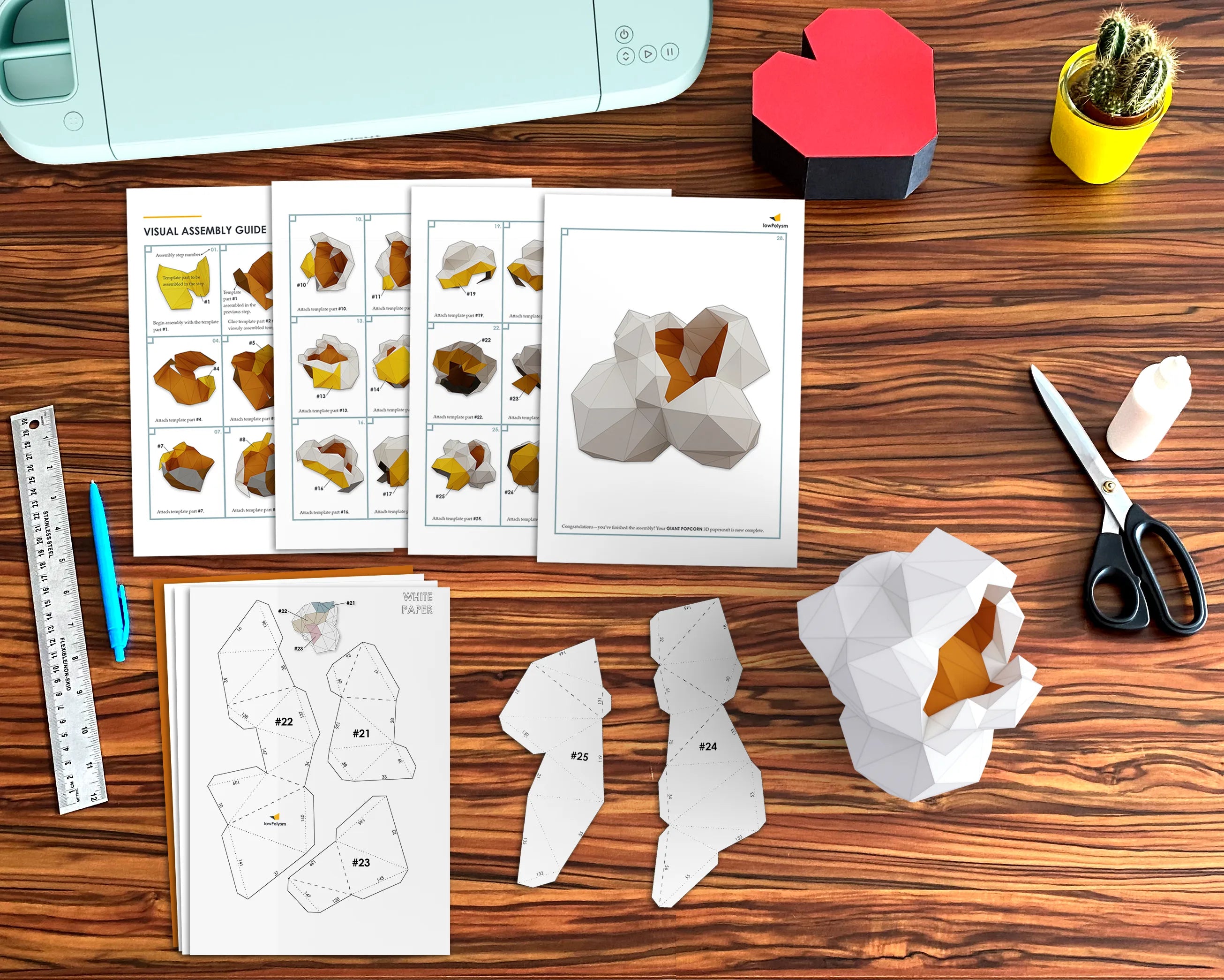 Desk with paper craft templates, scissors, cutting machine and a 3D popcorn paper model with assembly instructions.