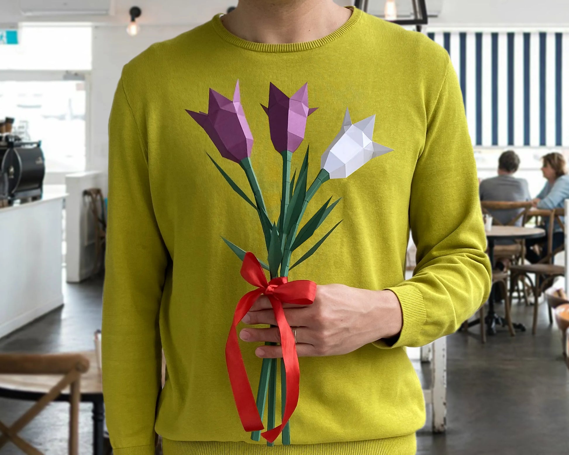 A person holding a handmade bouquet of purple and white paper bellflowers with a red ribbon, presented as a unique DIY gift.